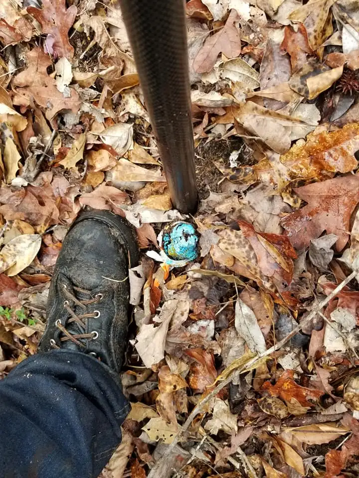 Surveyor’s boot next to a corner marker with a blue cap in the leaves