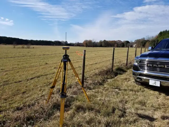 GPS rover on a tripod set up along a fence line in an open Alabama field